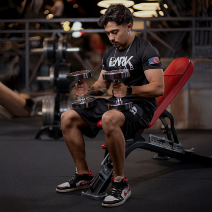 Homem sentado em aparelho da academia com pesos sobre as pernas usando a bermuda masculina e academia da Dark Lab