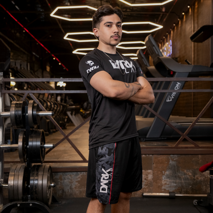 Homem na academia com braços cruzados de perfil usando a bermuda masculina Dark Lab que tem o logo da marca na parte lateral