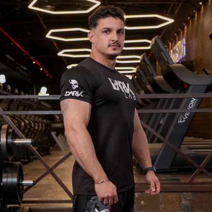 Homem de perfil na academia usando Camiseta de Caveira para Treino da Dark Lab que tem a logo da marca na região frontal e a caveira ícone da marca na manga