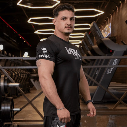 Homem de perfil na academia usando Camiseta de Caveira para Treino da Dark Lab que tem a logo da marca na região frontal e a caveira ícone da marca na manga