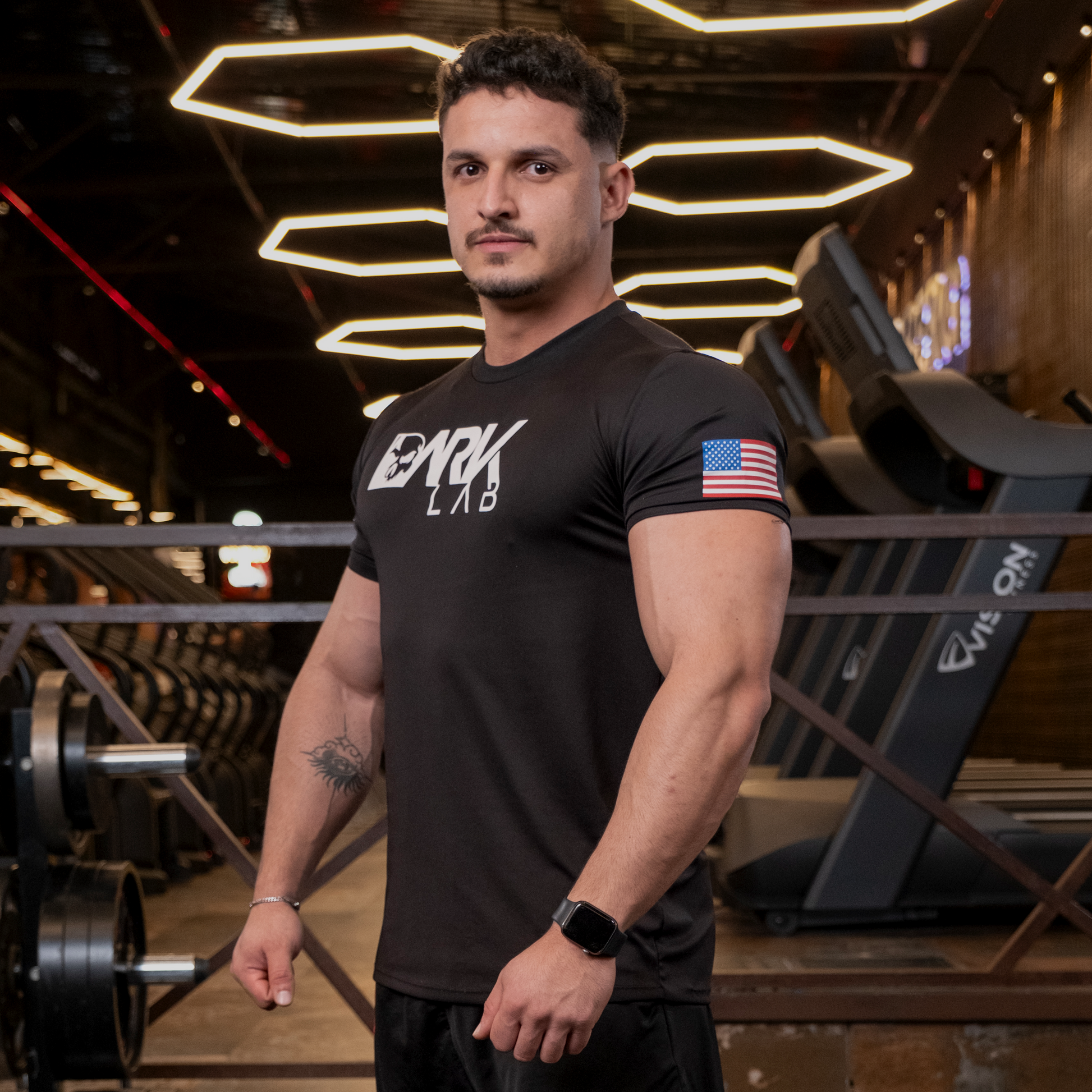 Homem de perfil na academia usando camiseta de caveira para Treino da Dark Lab mostrando o ícone da bandeira americana na manga.