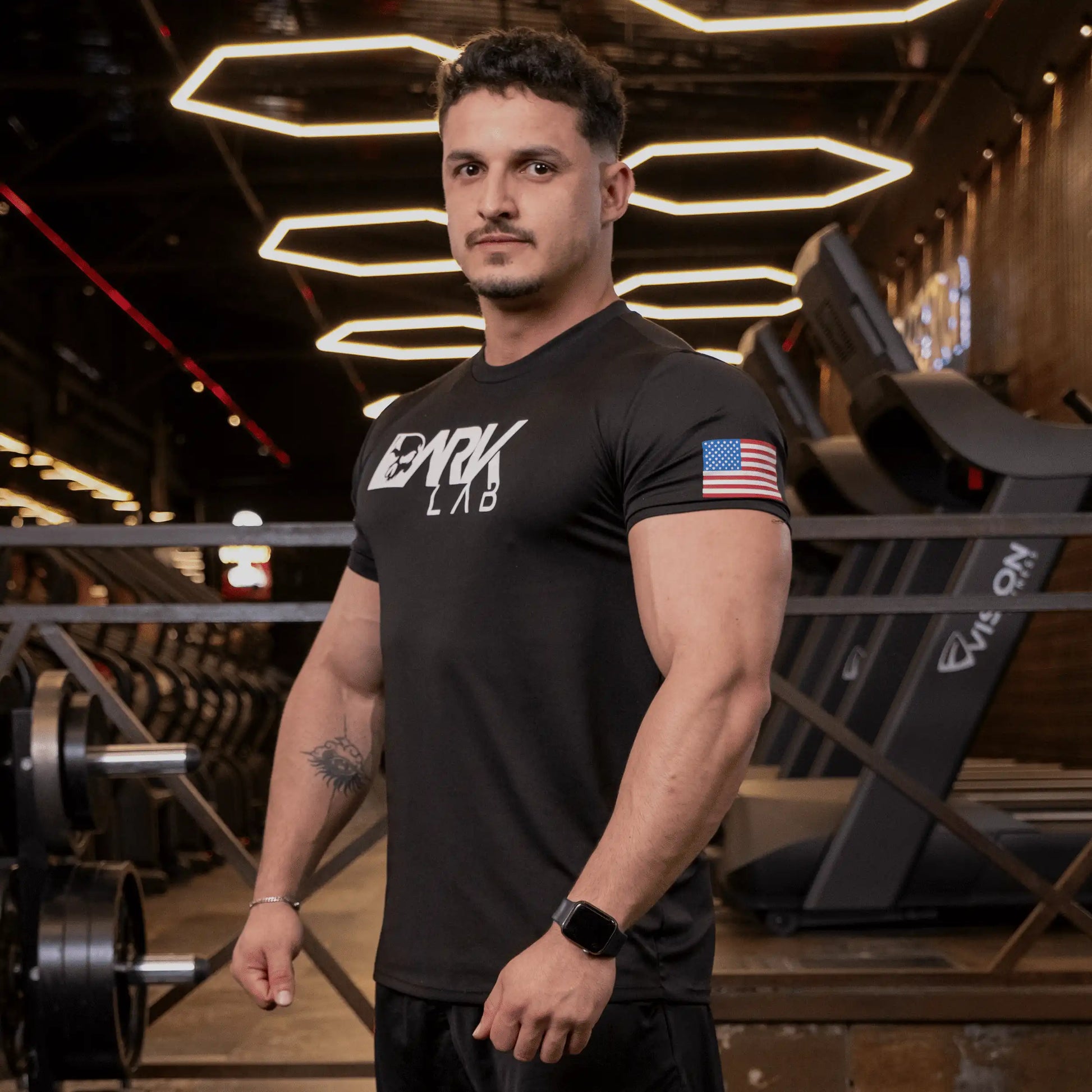 Homem de perfil na academia usando camiseta de caveira para Treino da Dark Lab mostrando o ícone da bandeira americana na manga.