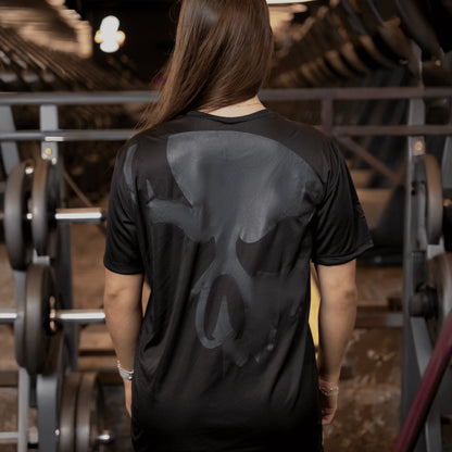 Mulher de costas na academia usando camiseta Dry-fit Preta de caveira da Dark Lab mostrando a parte de trás da camiseta que contém a caveira ícone da marca 