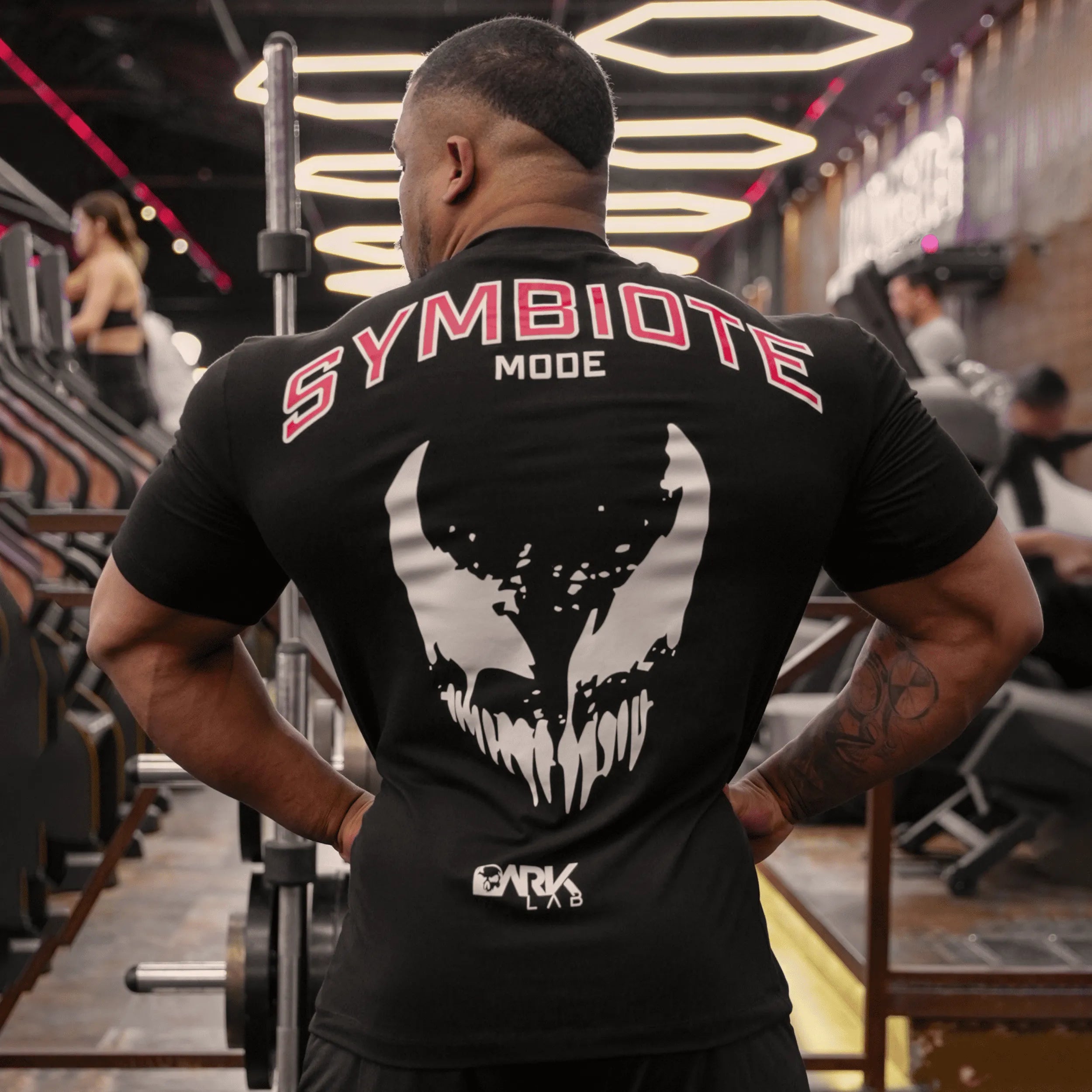 Homem de costas na academia usando a Camiseta Modo Simbionte da Dark Lab mostrando a parte de trás da camiseta com a escrita "Symbiote mode"