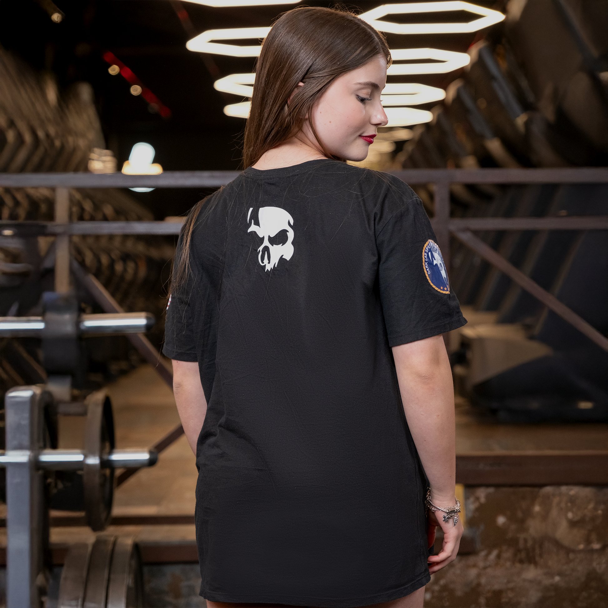 Mulher de costas na academia mostrando a parte de trás da camiseta para Academia Dark Force, com a caveira ícone da Dark Lab