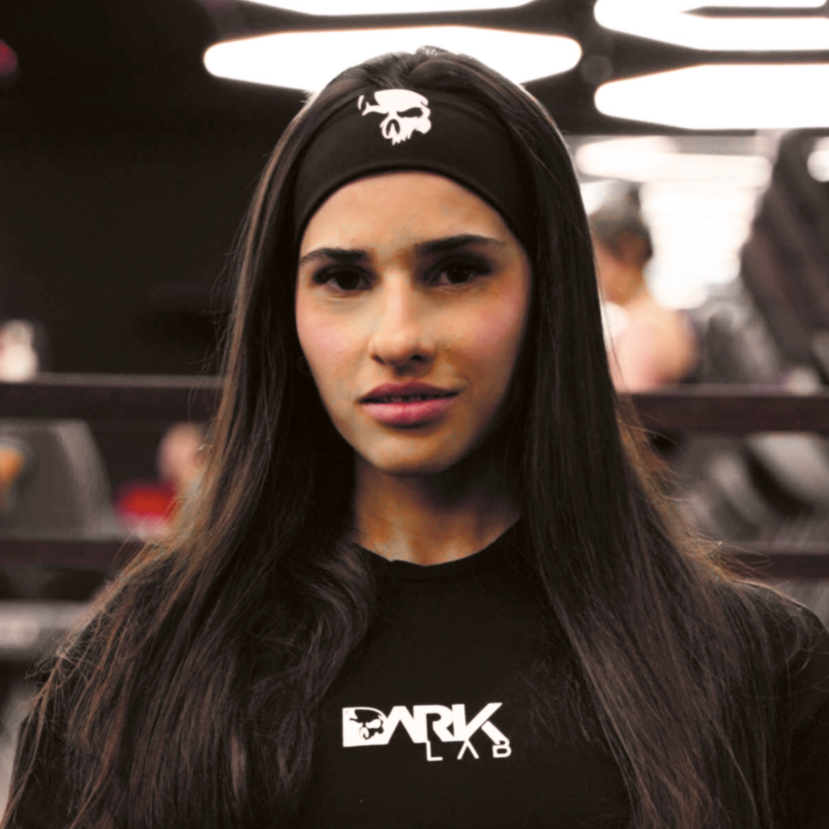 Mulher em ambiente de academia usando a faixa de cabelo para academia da Dark Lab e uma camiseta da marca